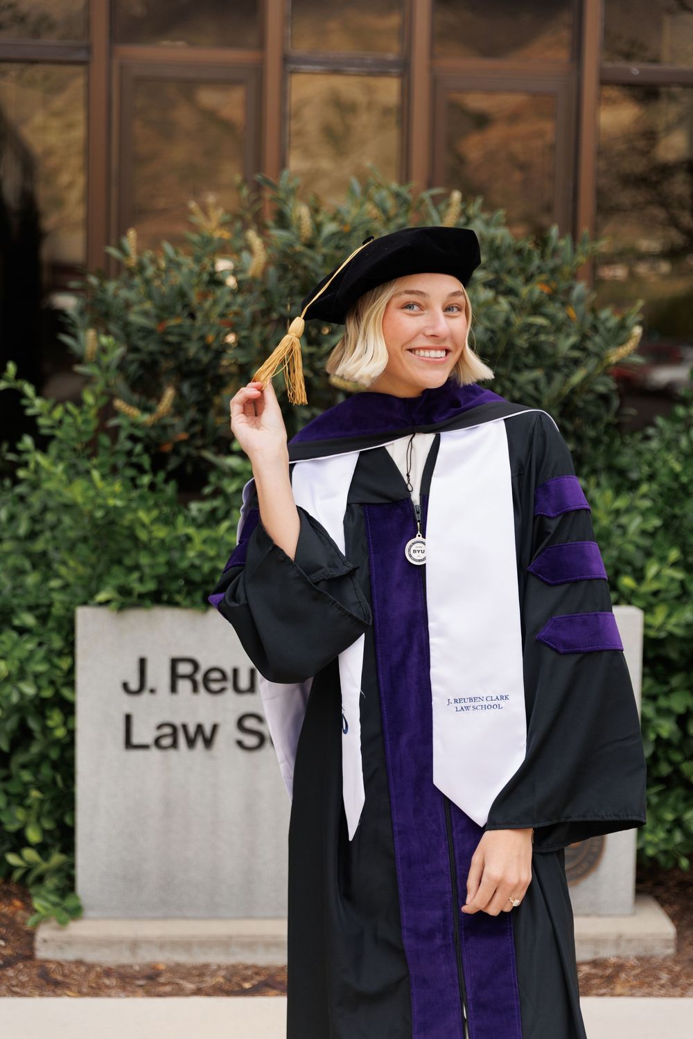 Smiling woman in law school graduation cap and gown outside J. Reuben Clark Law School.