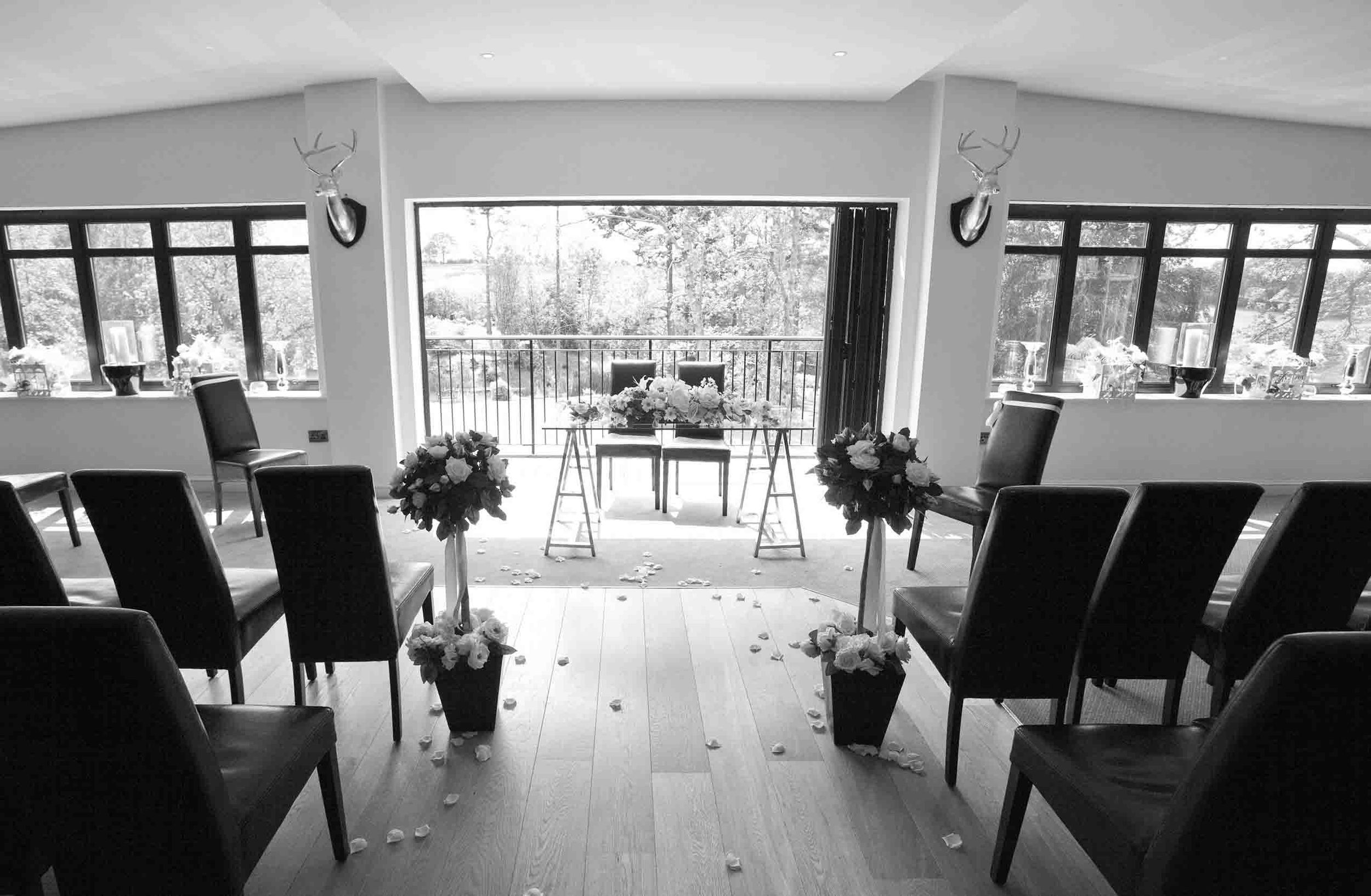 Black and white view down the Heather Glen wedding ceremony aisle, with rows of chairs and floral arrangements framing the windows.