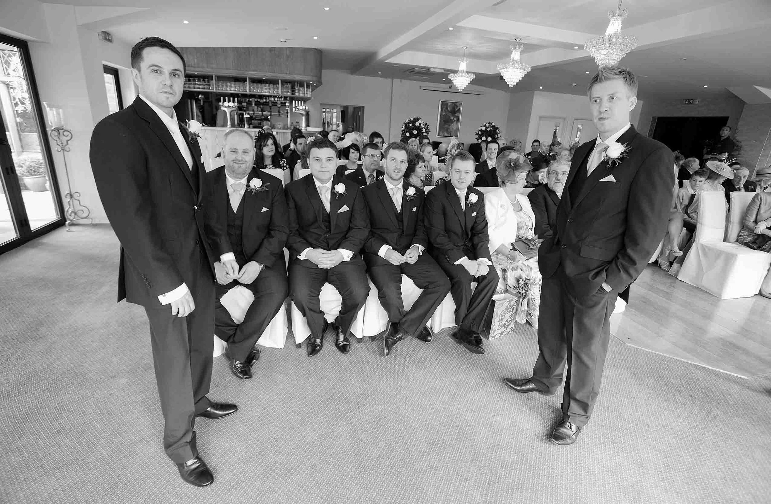 Groom waiting before his wedding ceremony at Heather Glen Country House Hotel, with seated guests behind him, in black and white.