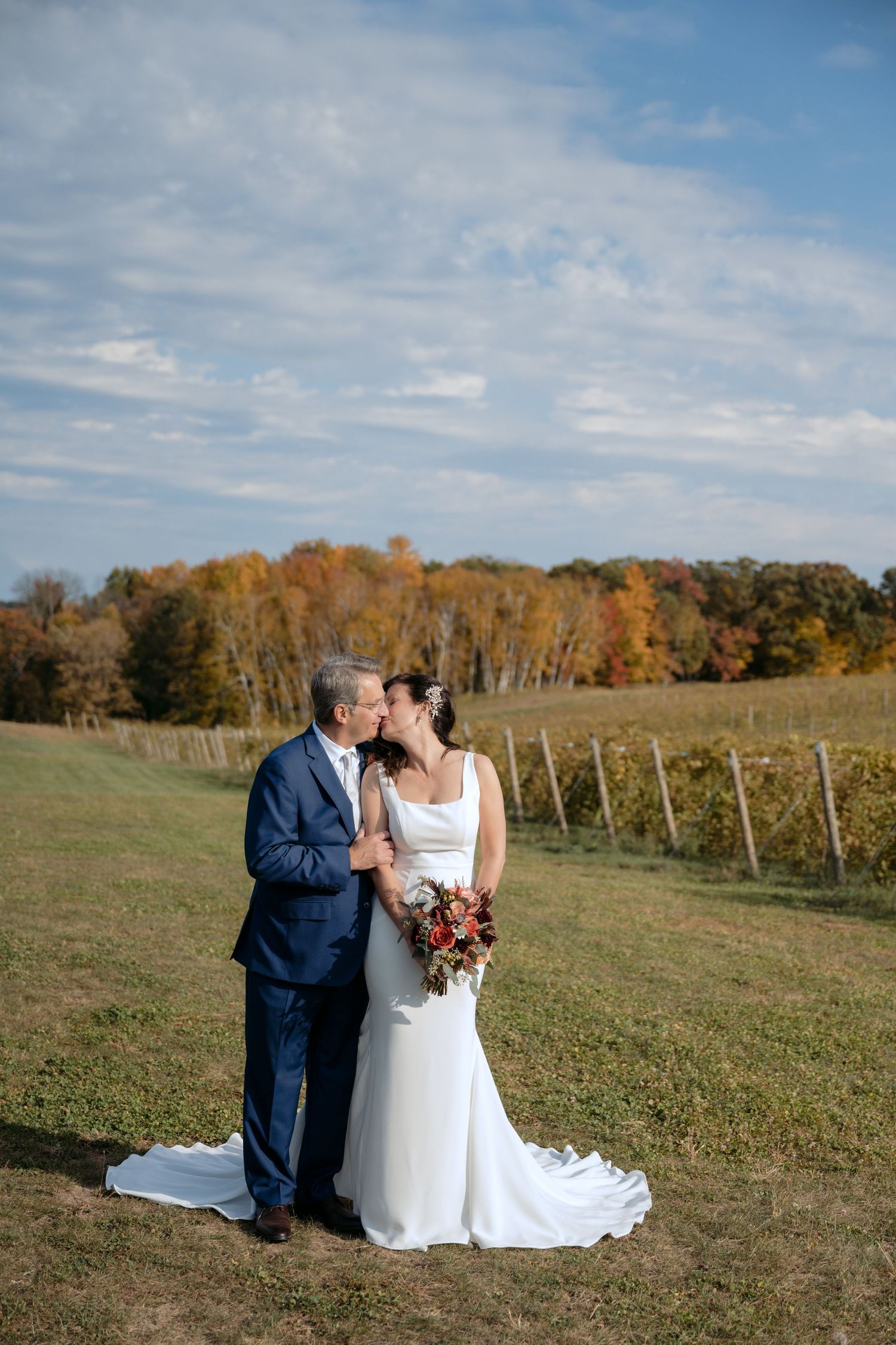 Bride & Groom kiss after their ceremony with rolling vineyard views and fall colors at Rustic Roots Winery in Scandia, MN.