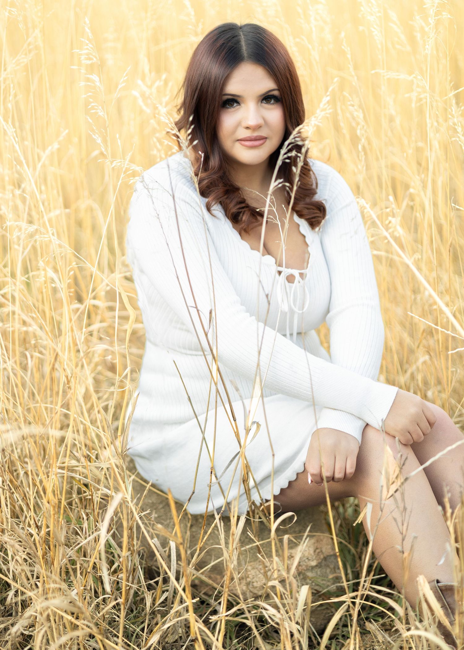 Young woman in white dress sitting gracefully among golden tall grass in a sunlit field.