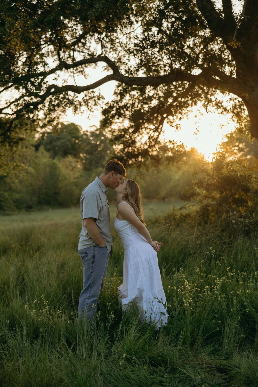 Couple kissing under oak tree during outdoor engagement session in Georgia.