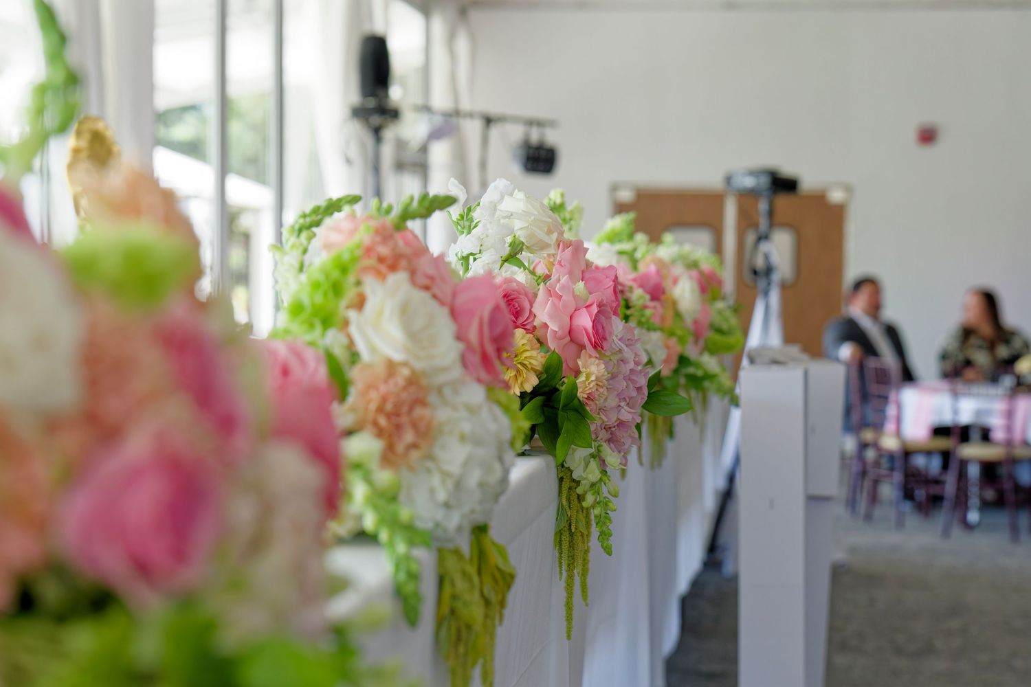 Elegant pink white and green floral arrangements decorating white pew ends at quinceañera reception venue.