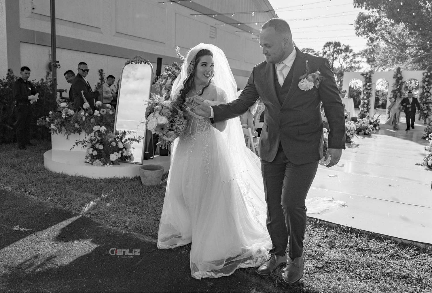 Black and white photo of a bride and groom walking down the aisle at an outdoor wedding ceremony.