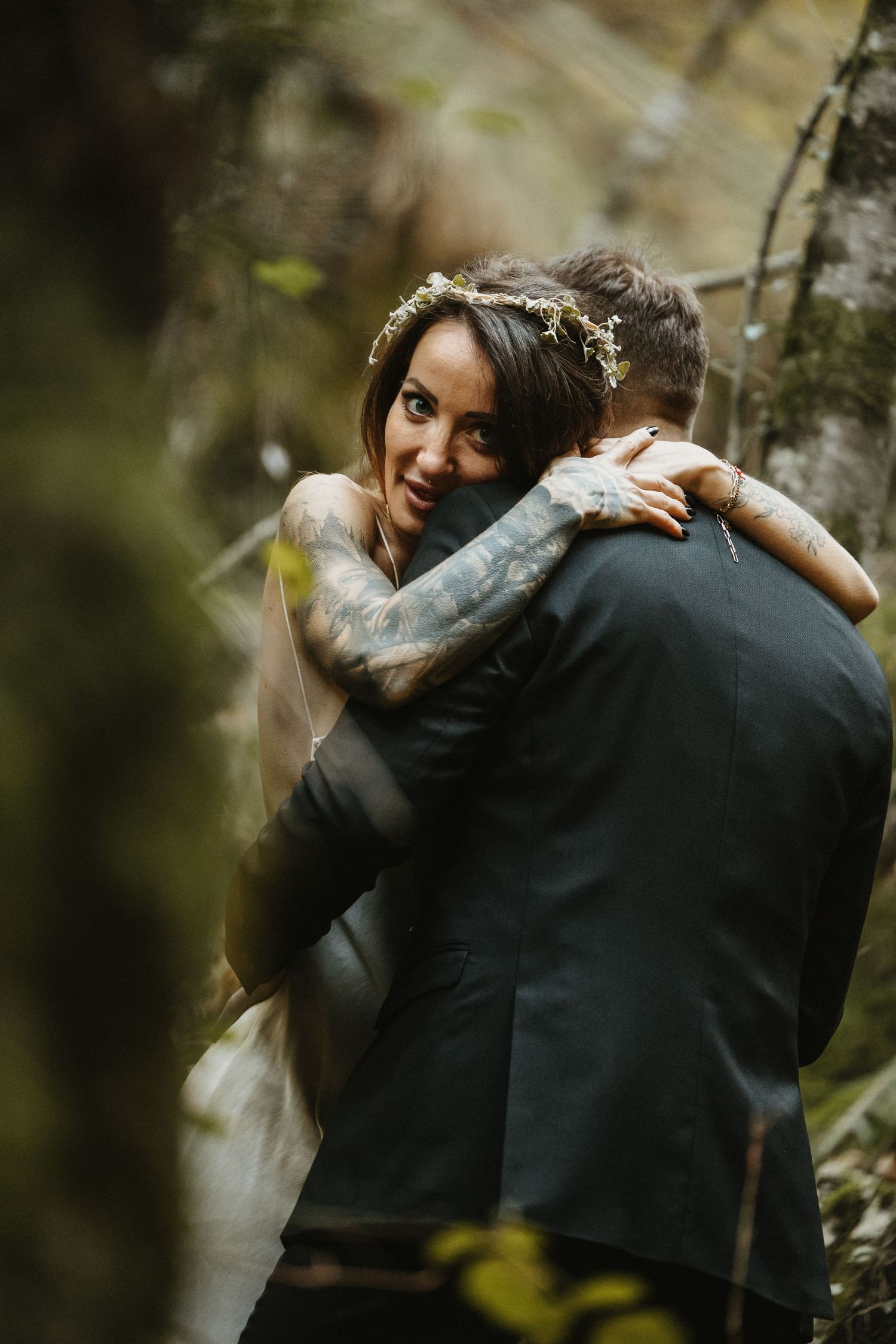 A bride embraces the groom in a forest setting.