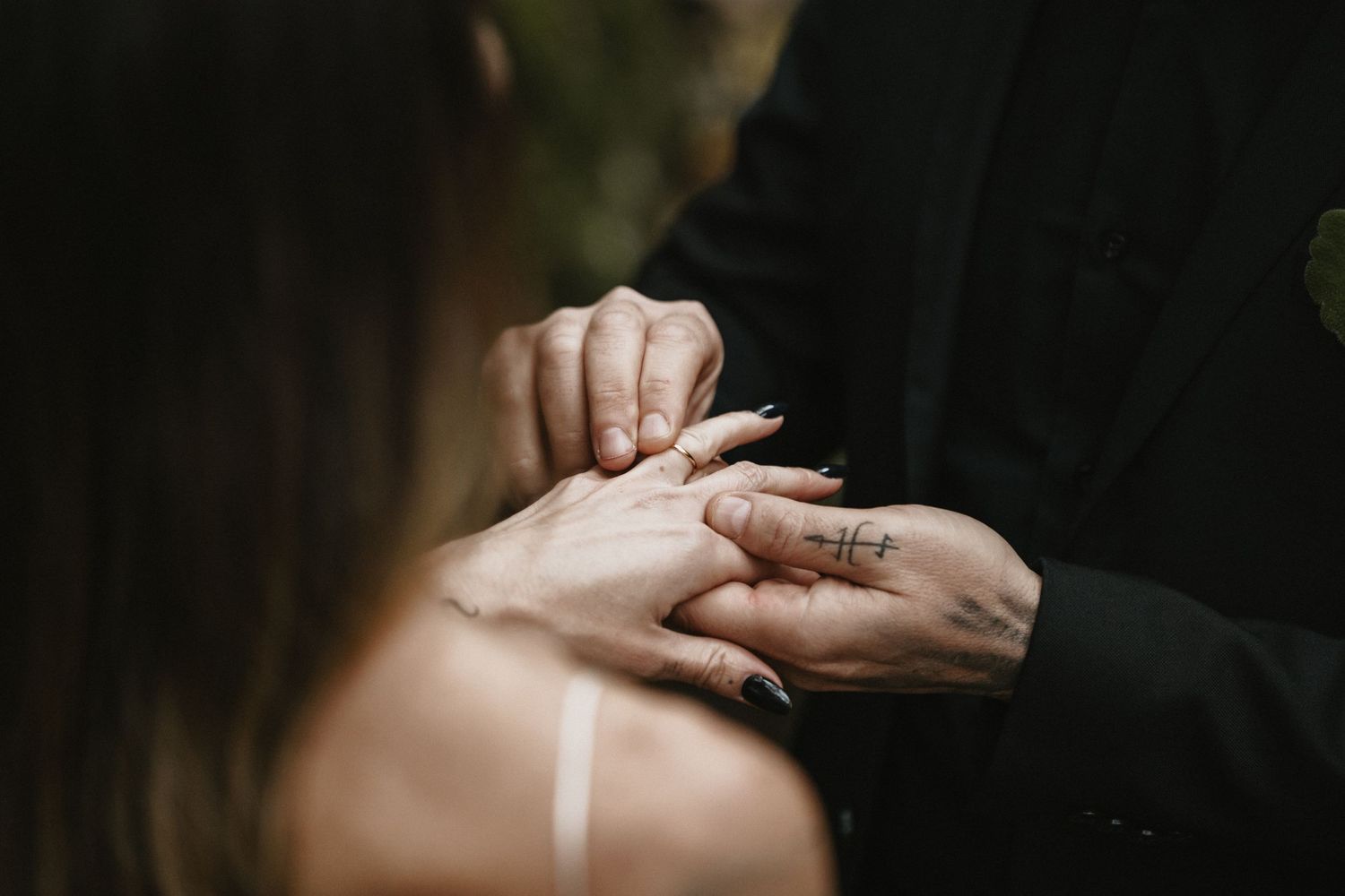 Close-up of a groom placing a wedding ring on the bride’s finger outdoors.