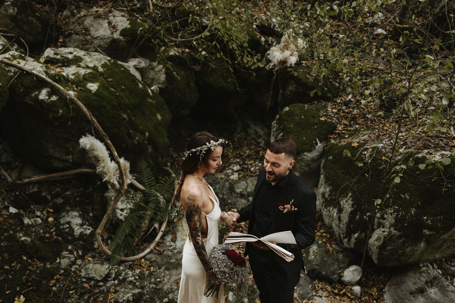 Bride and groom stand together among mossy boulders in a forest.