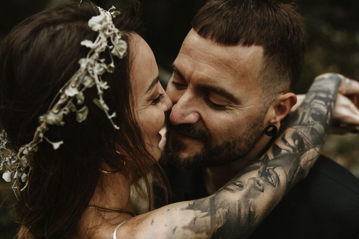 Couple sharing a kiss with bride wearing floral crown in woodland setting.