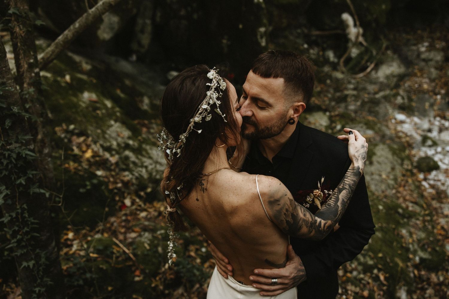 Bride and groom sharing a romantic kiss in an autumn forest backdrop.