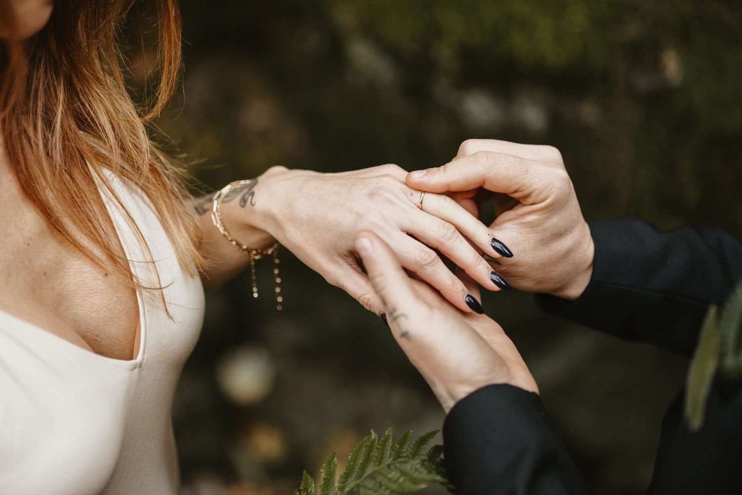 Close-up of groom placing wedding ring on brides finger outdoors.