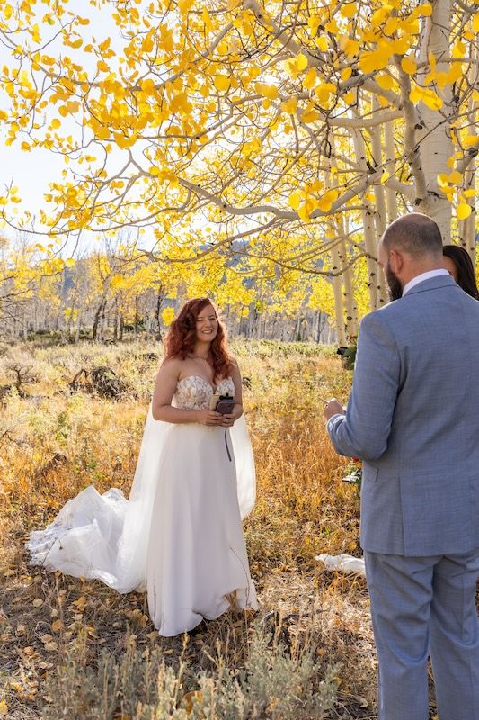 Bride and groom exchange vows outdoors among golden aspen trees during a fall wedding ceremony in Colorado.