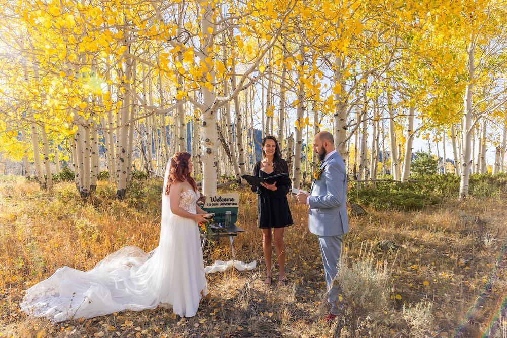 Couple exchanges vows with officiant among golden aspen trees during an outdoor fall wedding ceremony in a forest.