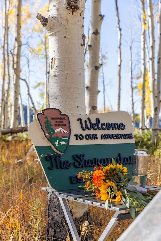 National Park Service welcome sign reading Welcome to Our Adventure amid autumn aspen trees with sunflower bouquet decoration.