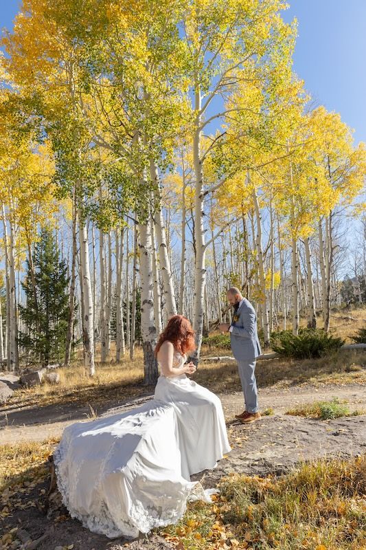 Bride and groom share a romantic moment among golden aspen trees during a fall outdoor wedding ceremony.