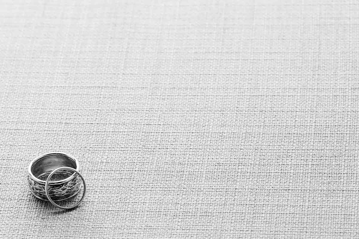 Black and white photo of stacked wedding rings resting on a textured linen fabric surface at the Inn on the Lake