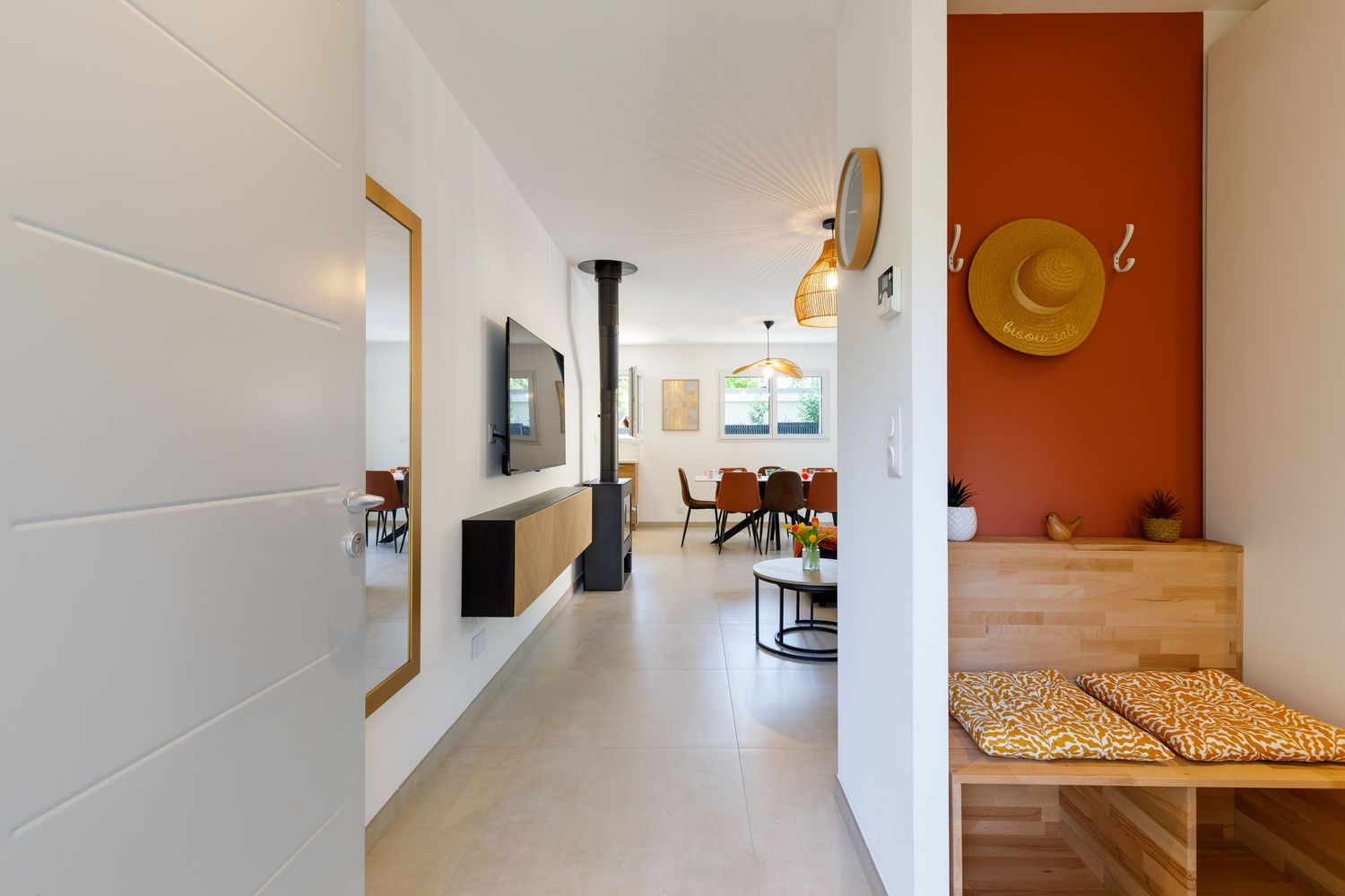 Entrée avec murs blancs, mur d'accent en terre cuite, banc en bois, poêle noir et espace salle à manger ouvert en arrière-plan.