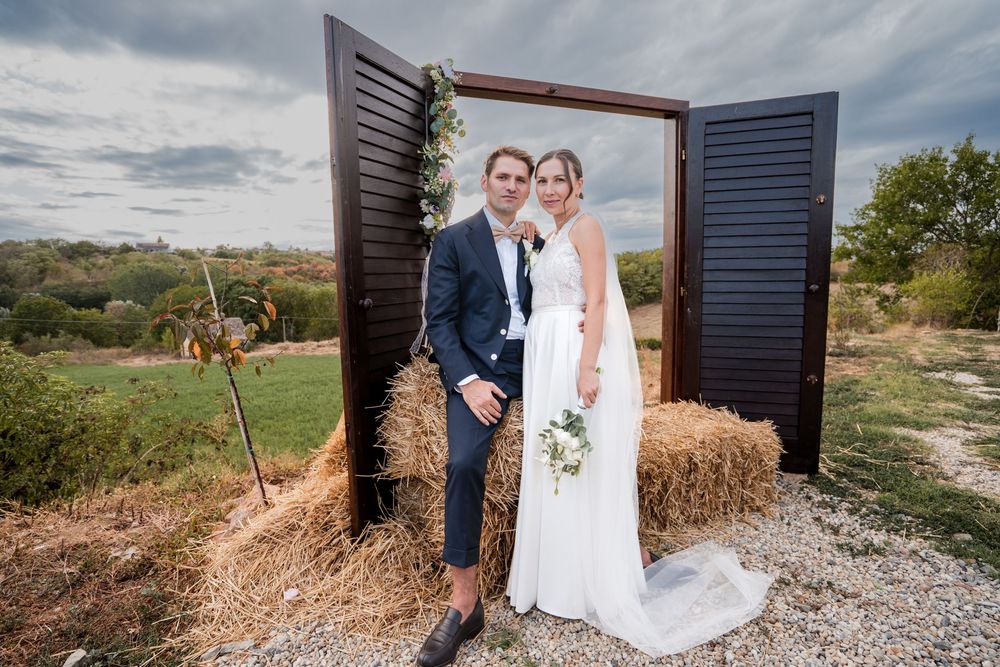 Bride and groom posing in front of rustic wooden doors on hay bales at an outdoor wedding ceremony.