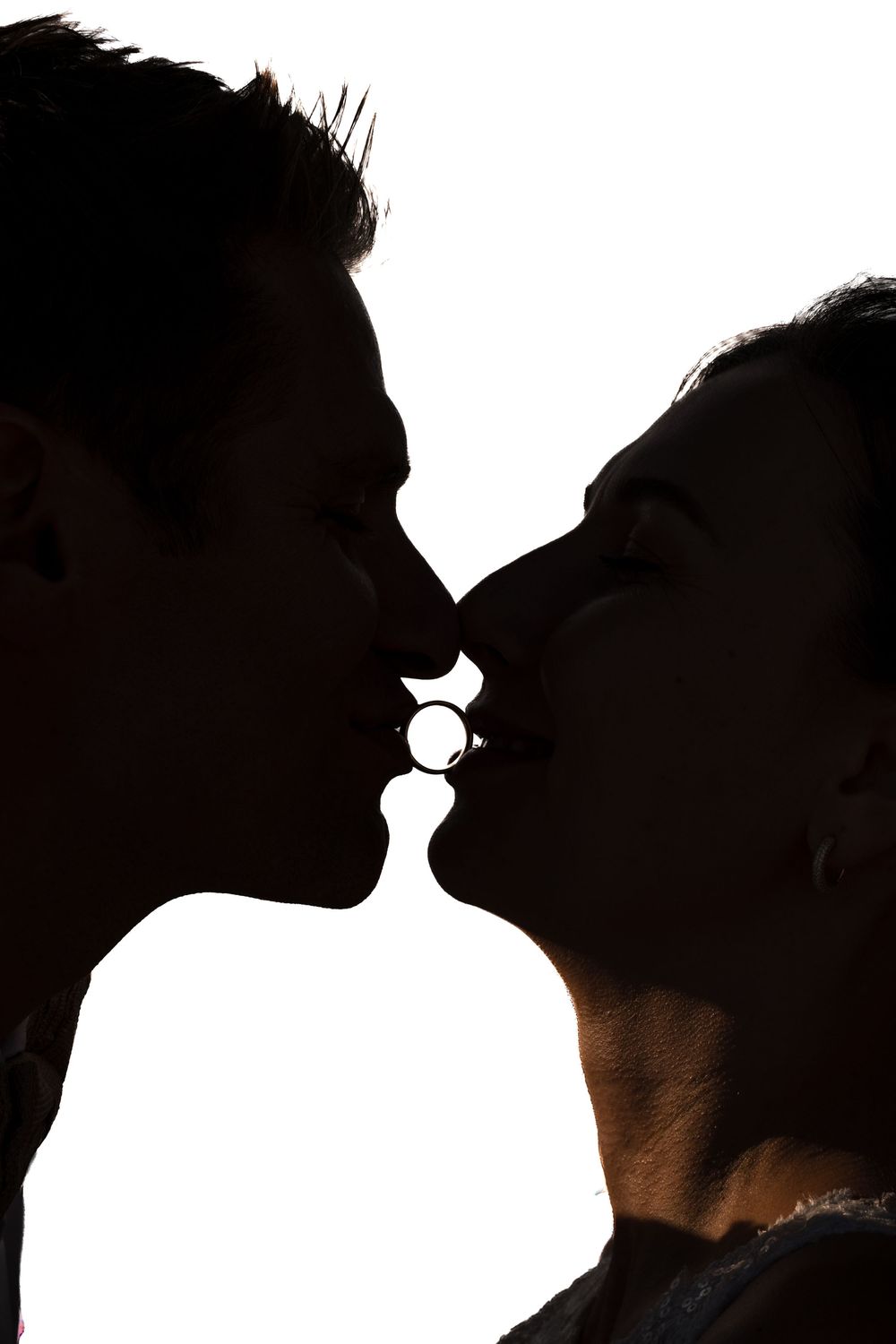 Silhouette of a romantic couple sharing a kiss against a bright white background.