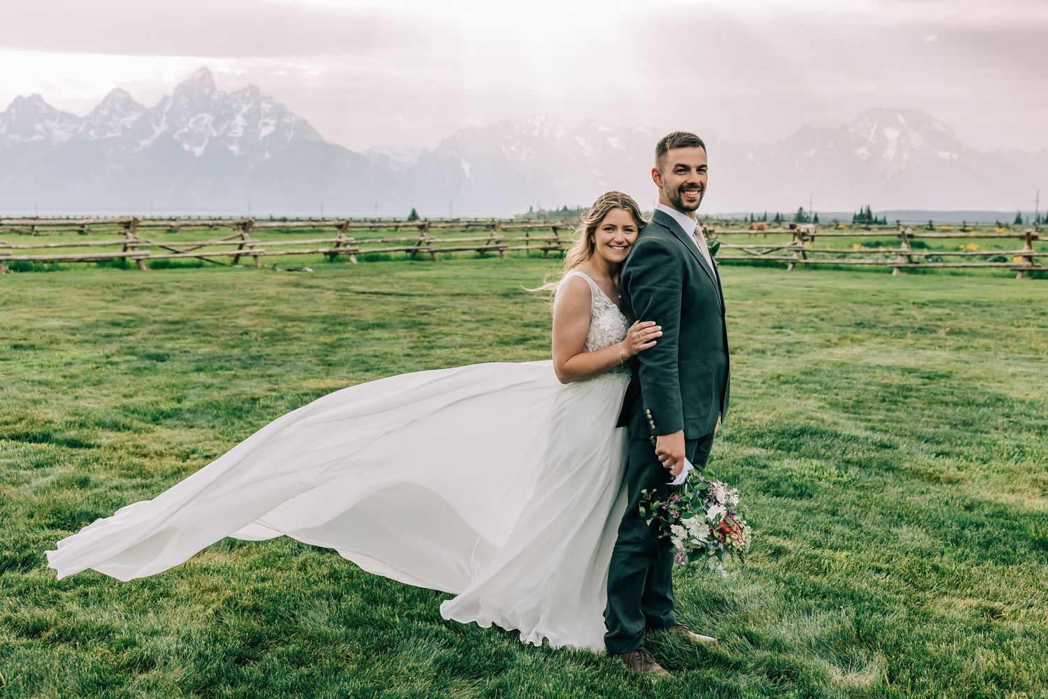 Mollie and Derek posing together in a grassy field with the Teton mountains behind them during their Jackson Hole elopement.