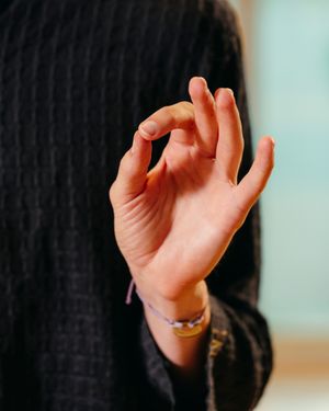 Close-up of a hand forming a mudra gesture with thumb and index finger touching, wearing a beaded bracelet and a dark knit sweater.