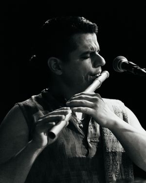 Black and white photo of a musician with closed eyes playing a flute beside a microphone during a live performance.