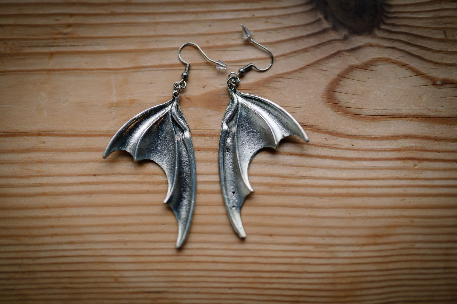 Silver bat wing earrings by Scarlet in Chains on a wooden table, worn by a gothic bride