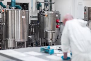 Stainless steel industrial tanks in a sterile pcb paint manufacturing facility with a lab technician in white protective gear.