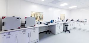 Modern sterile laboratory interior with white cabinets, workbenches, lab equipment, and incubators in a clean facility.