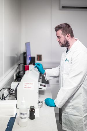 A lab technician in a white coat and blue gloves operates scientific equipment in a modern laboratory setting.