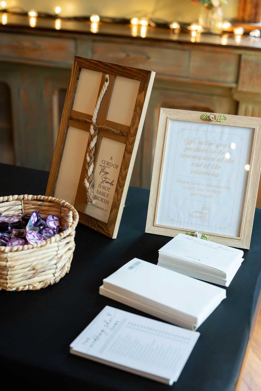 Wedding guest book table with framed signs, notecards, and a wicker basket of favors, decorated with candlelight.