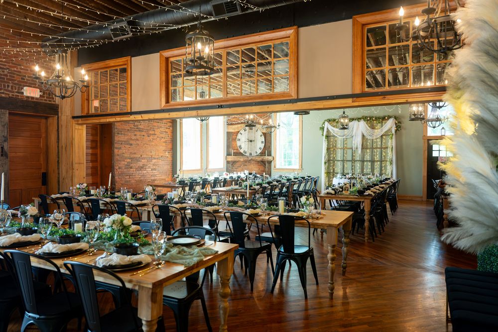 Elegant wedding reception venue with long wooden tables, black chairs, brick walls, and chandelier lighting.