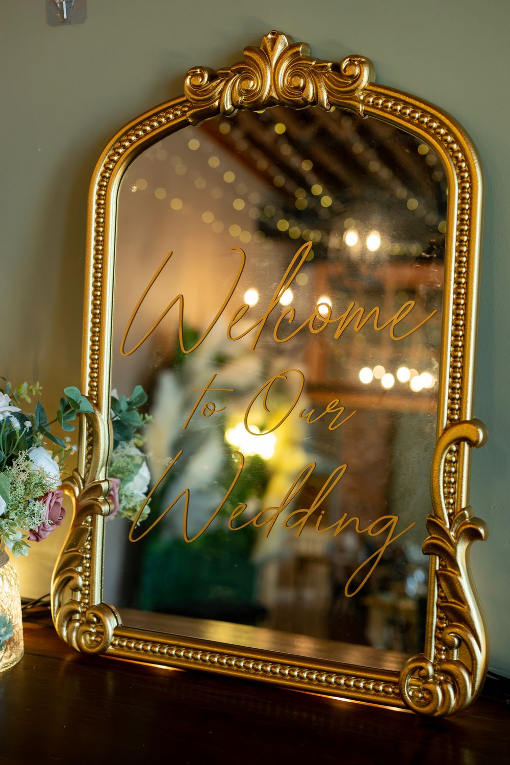 Gold ornate mirror with cursive Welcome to Our Wedding sign at elegant wedding venue reception.