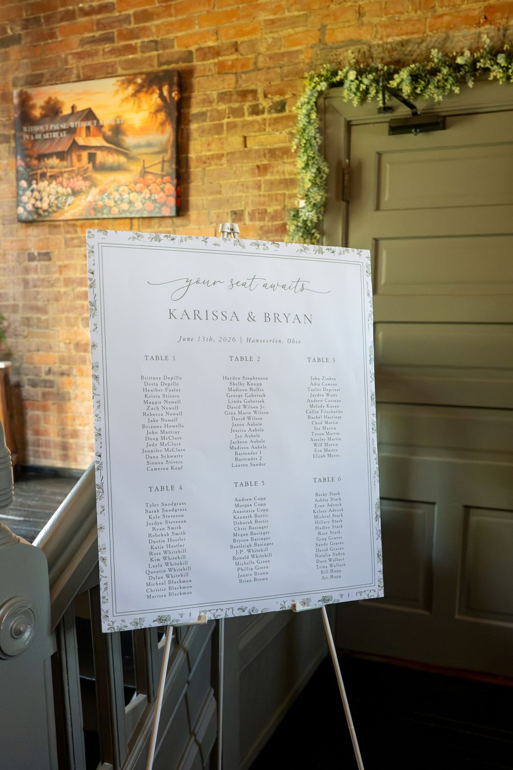 Elegant wedding seating chart on easel for Karissa and Bryan, displayed in a rustic venue with brick walls and green decor.