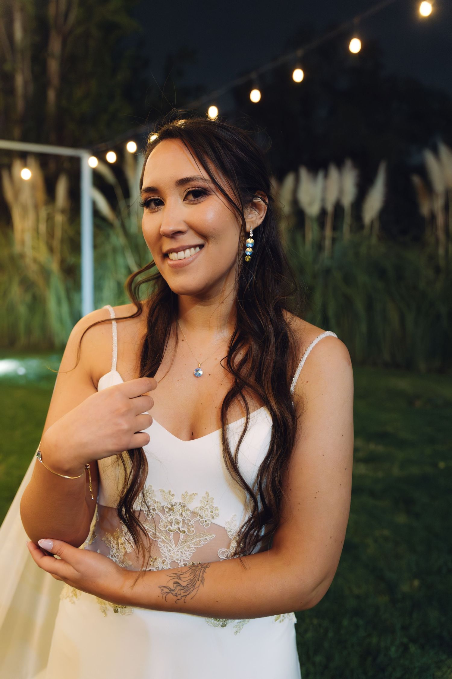 Radiant bride smiles beautifully in a white gown with lace detail and elegant jewelry at her evening wedding.