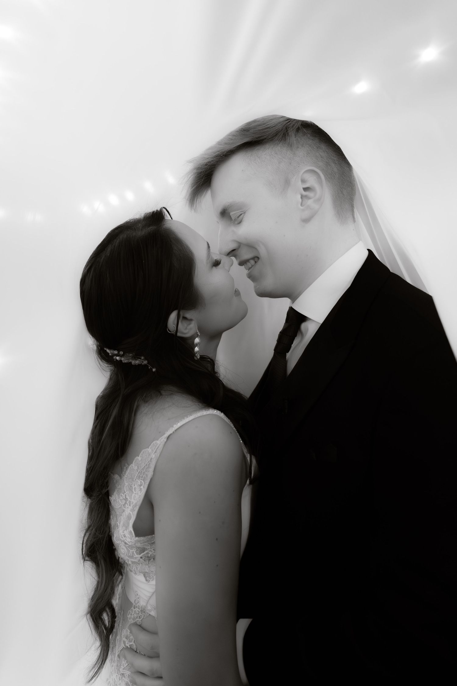 Black and white intimate portrait of bride and groom sharing a romantic moment under wedding tent.