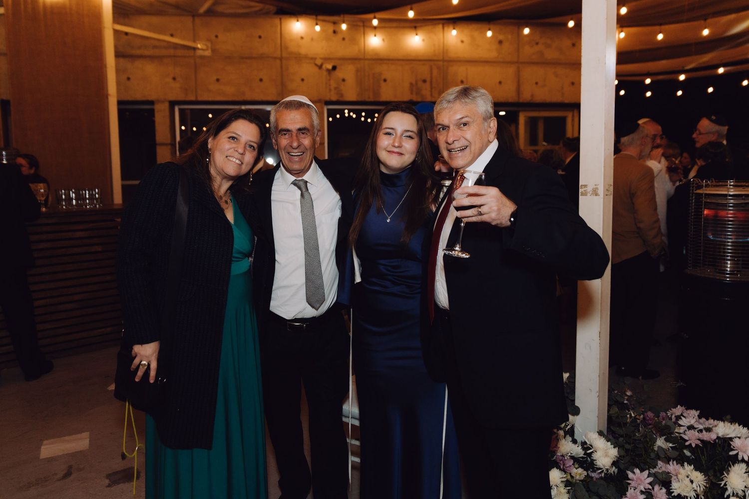 Two couples posing together at a festive evening wedding reception with floral decorations.