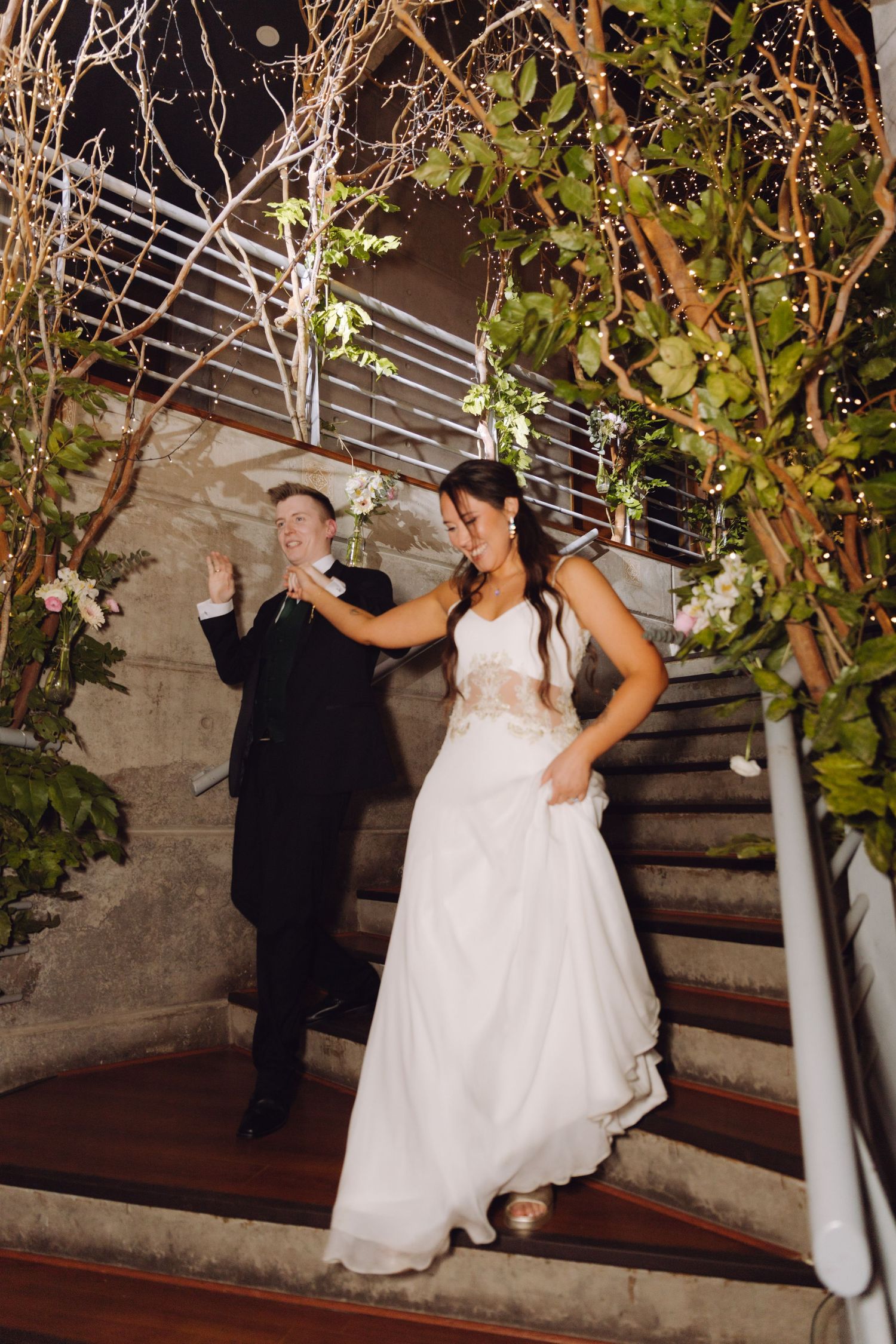 Bride and groom descending decorated staircase with floral arrangements at their wedding reception.
