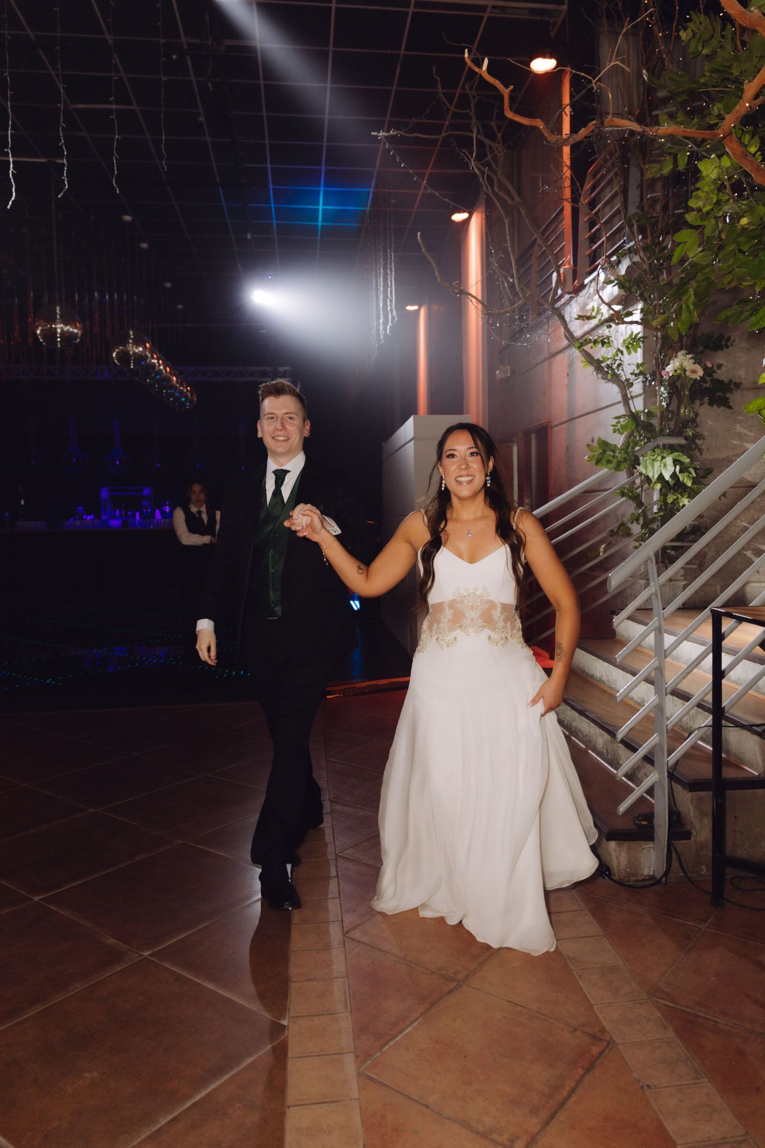 Bride in white gown and groom in black suit making grand entrance at wedding reception.