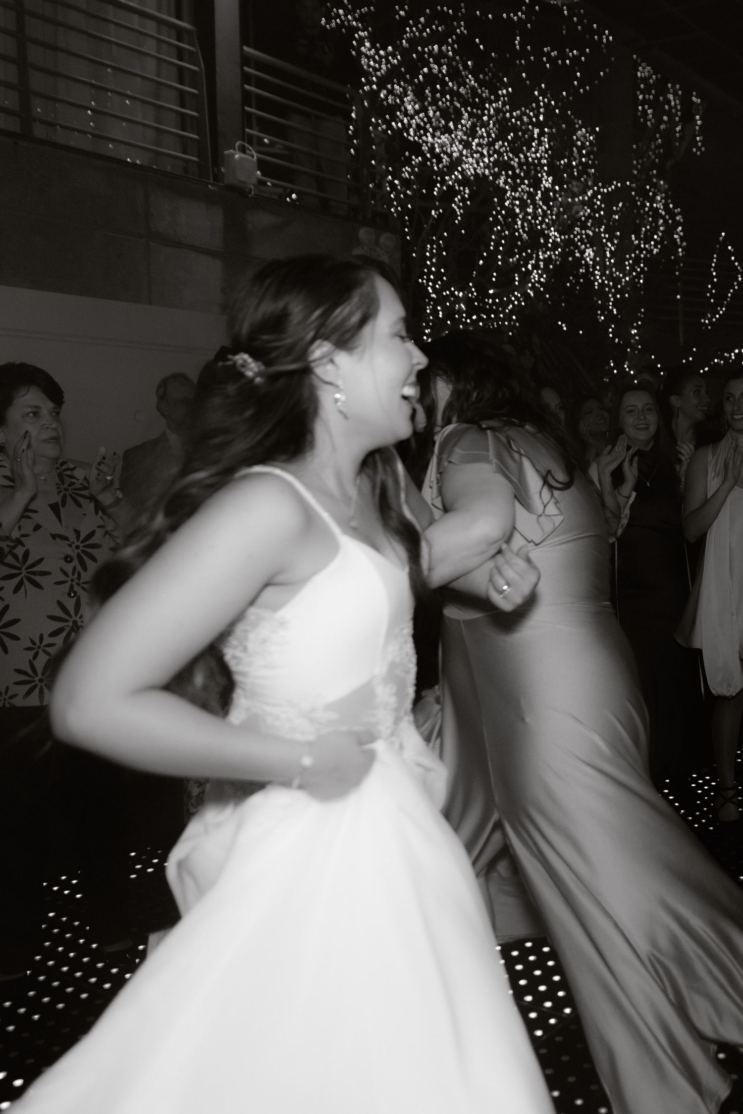 Black and white photo of bride dancing joyfully with guests on sparkling dance floor.