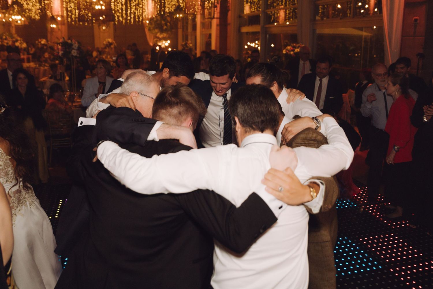 Wedding guests forming a group hug circle on a starlit dance floor at reception.