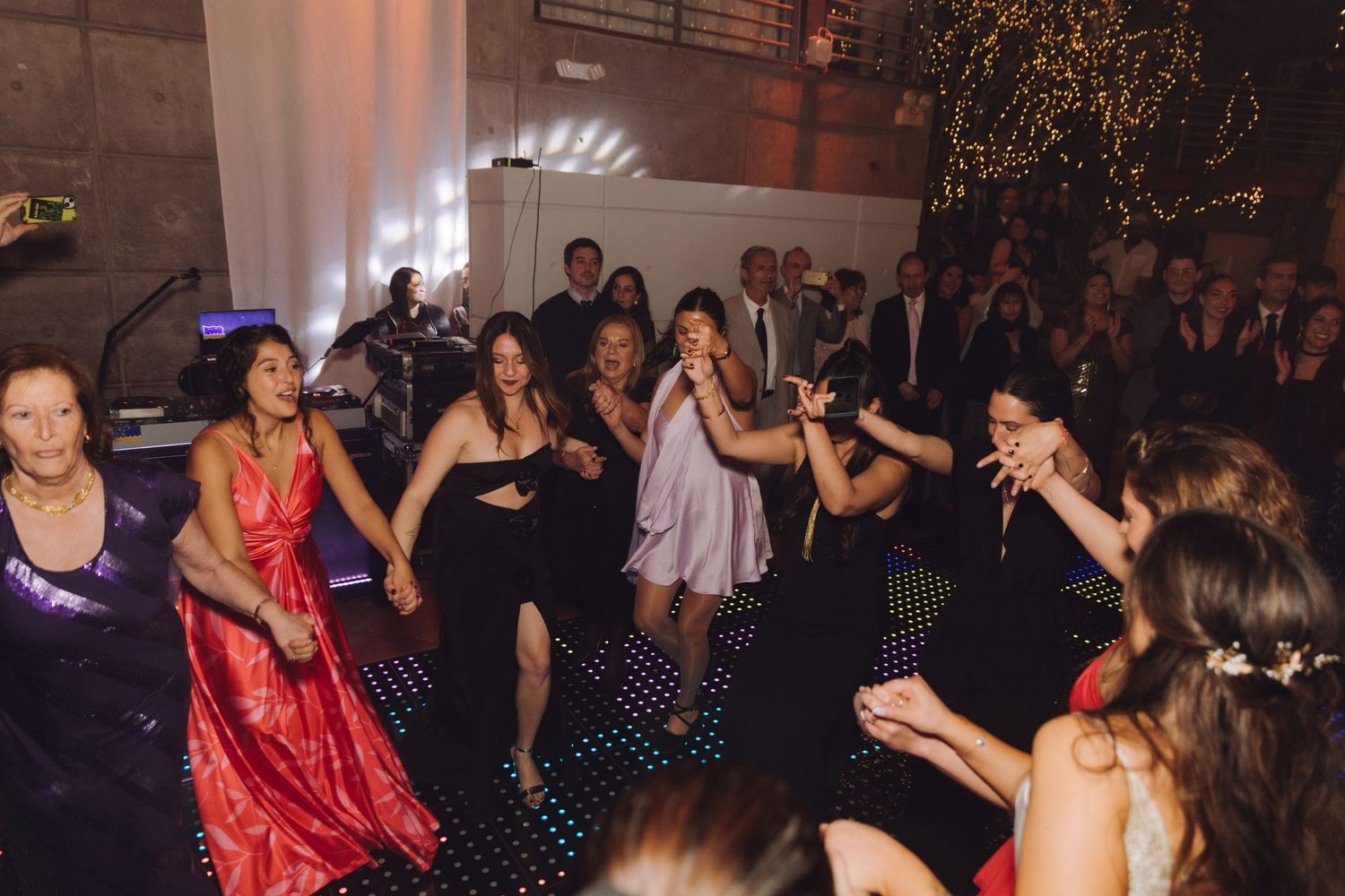 Energetic group of women dancing together on a dark dance floor at wedding reception.