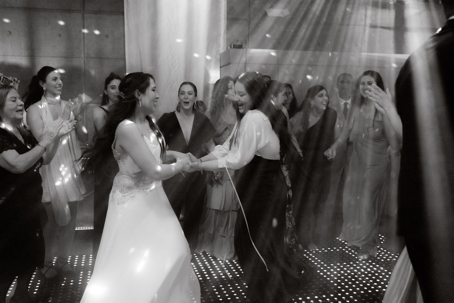 Bride and guest hold hands dancing on a sparkling dance floor at an elegant wedding reception.