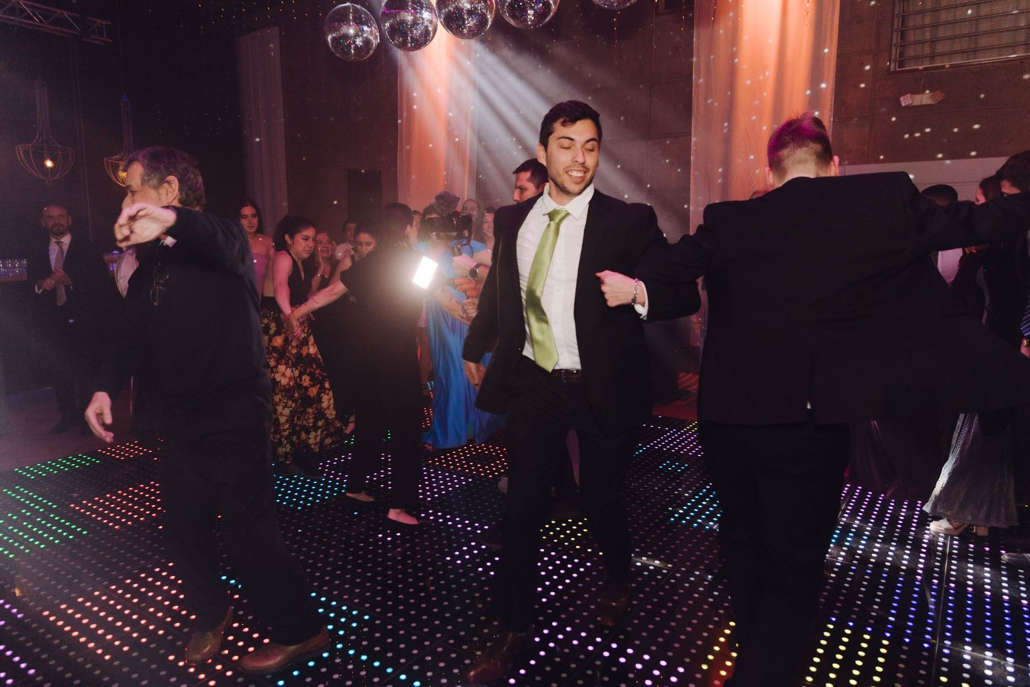 Man in suit with green tie dancing energetically on a LED dance floor at a wedding reception.