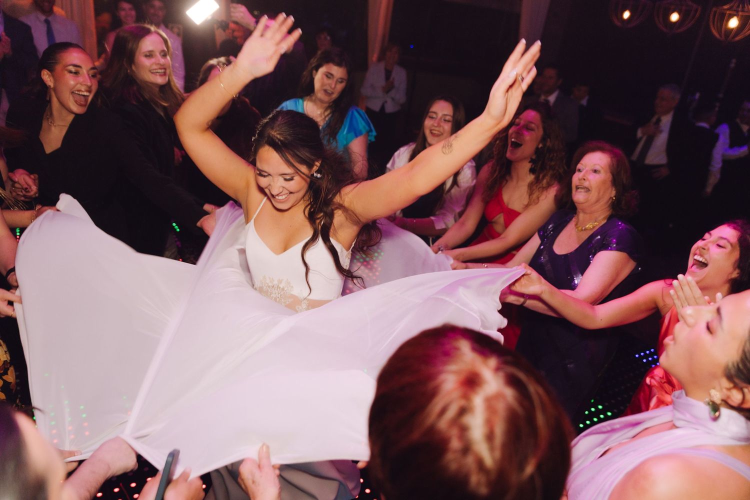 Radiant bride twirling her white gown with arms raised surrounded by cheering wedding guests.