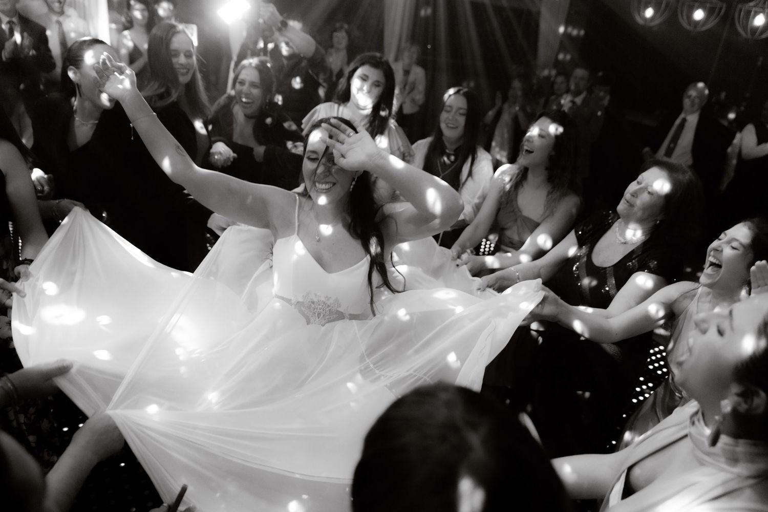 Black and white photo of bride dancing with sparklers and guests lifting her wedding veil.