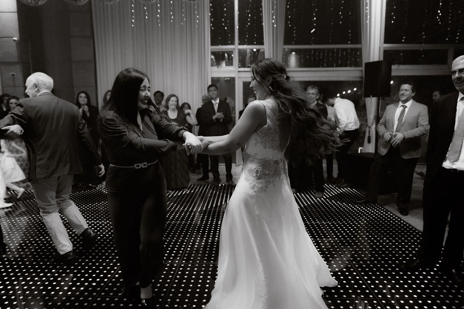 Black and white photo of bride dancing with a guest on a checkered wedding dance floor.