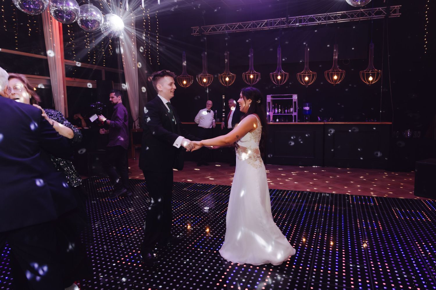 Bride and groom dancing together on star-lit dance floor surrounded by guests and disco balls at wedding reception.