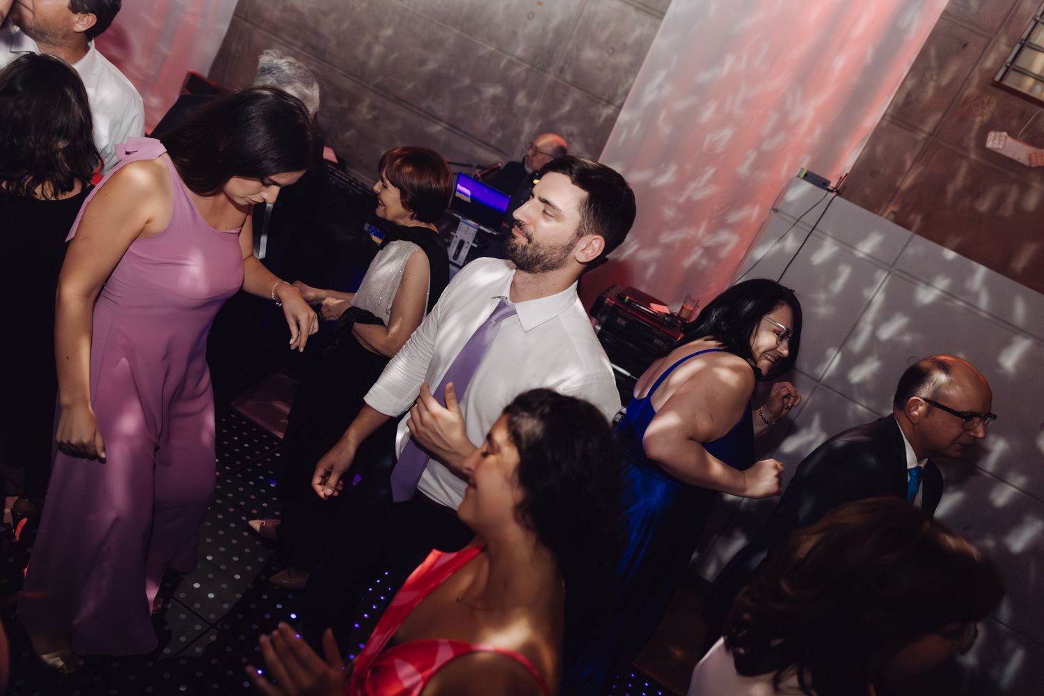 Wedding guest in white shirt dancing enthusiastically among colorfully dressed guests on the reception dance floor.