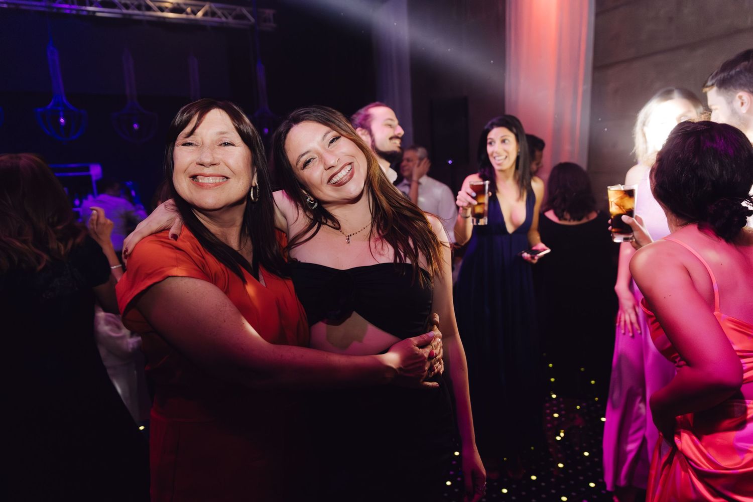 Two smiling women embracing and posing together on the dance floor at a vibrant wedding reception party.
