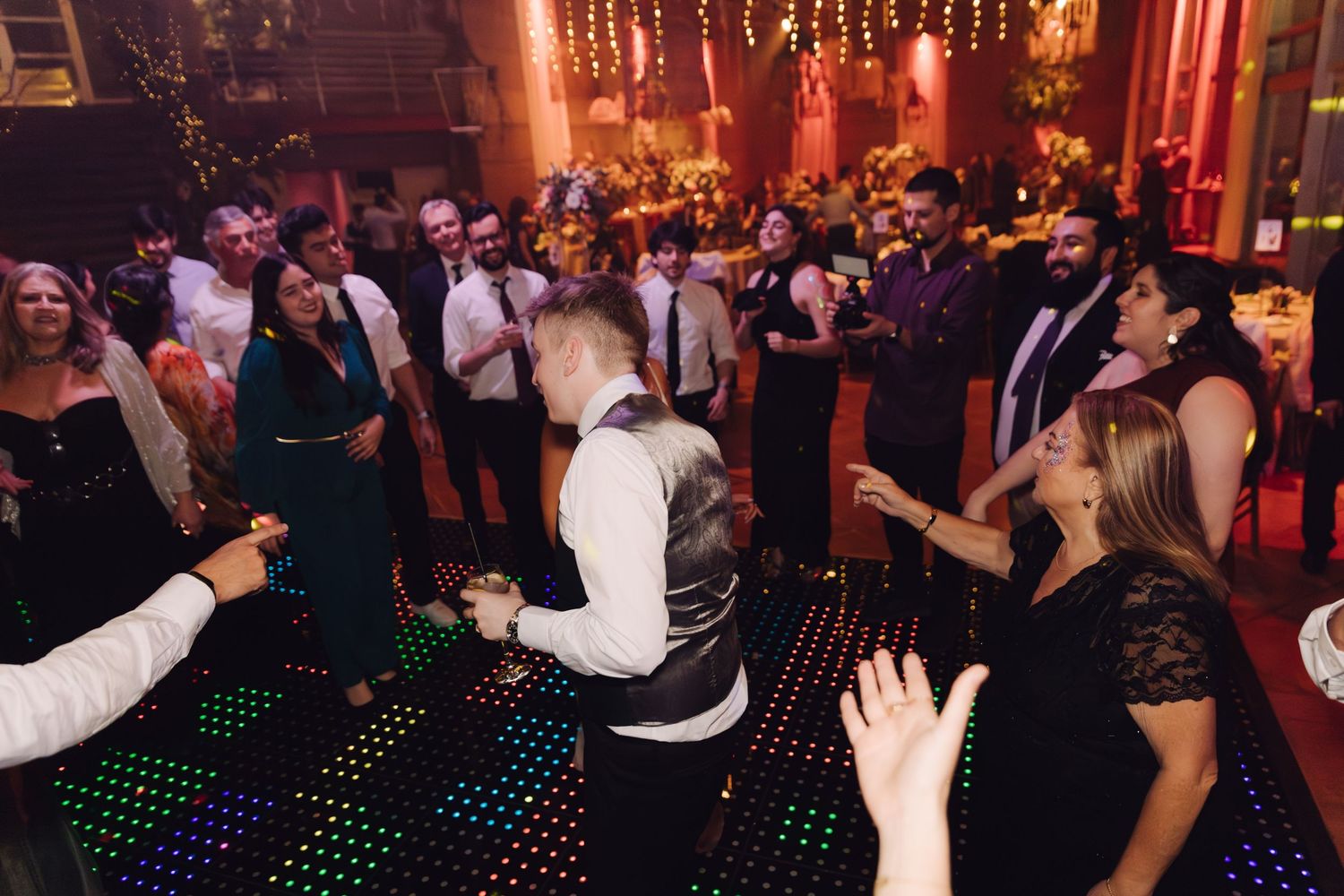 Wedding guests dancing on illuminated LED dance floor at elegant indoor wedding reception.